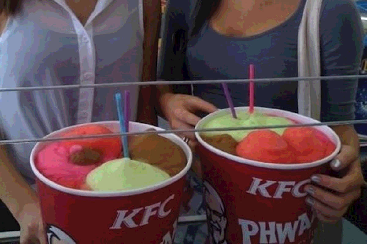 Two people showing off their fried chicken buckets used to hold Slurpee mixes during 7-11 bring your own Slurpee cup day.