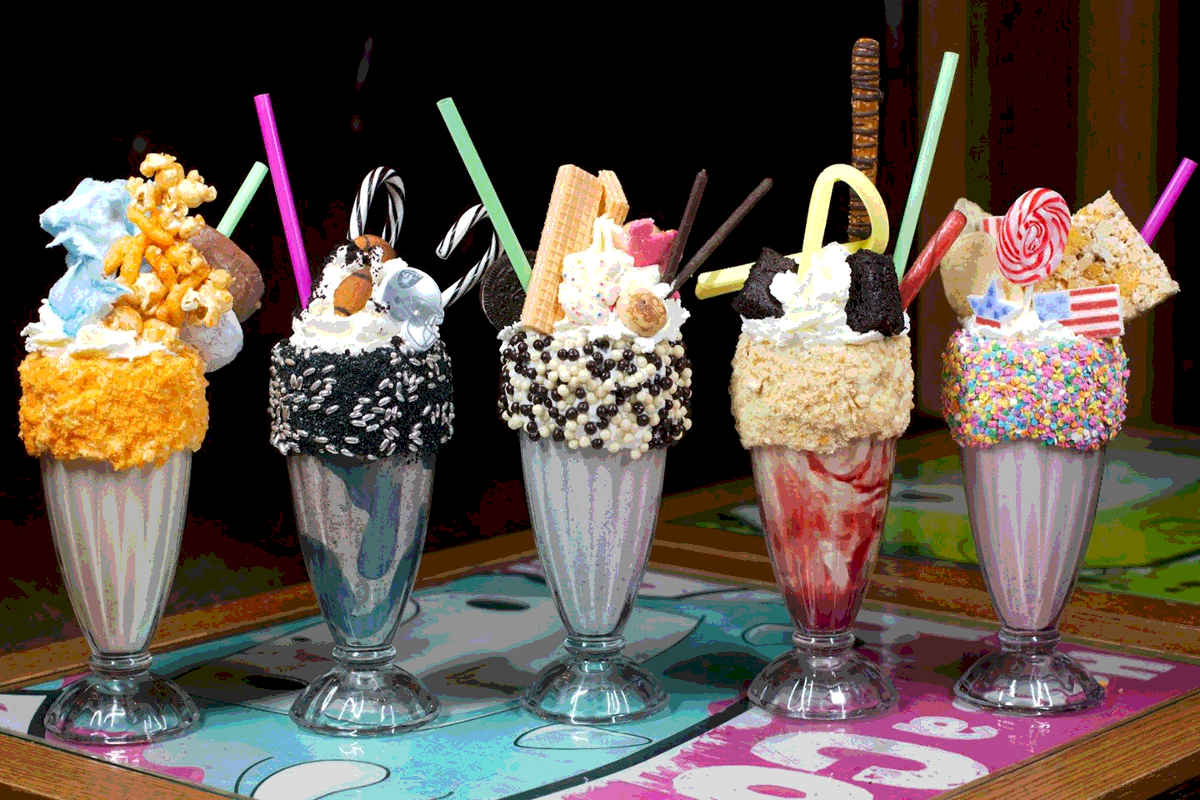 An array of five ornately decorated milkshakes with candy and other edibles