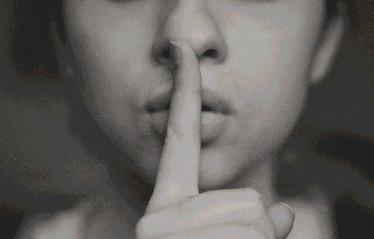 A woman indicating a secret with her index finger pointed up over her closed mouth