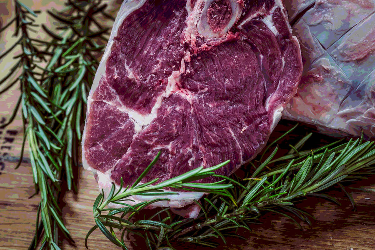 A cut of bone-in raw steak with rosemary on the sides
